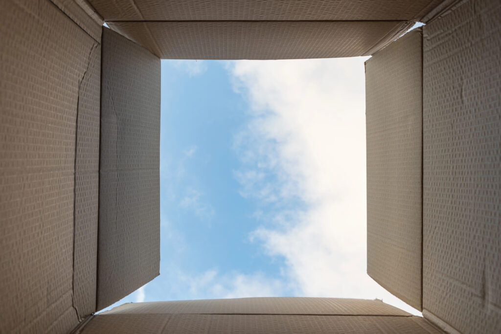 Open corrugated box with blue sky and clouds above